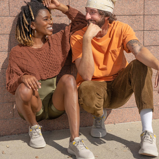 Young woman and man kneeling against the wall smiling at each other wearing SNNCE Tabi Sneakers