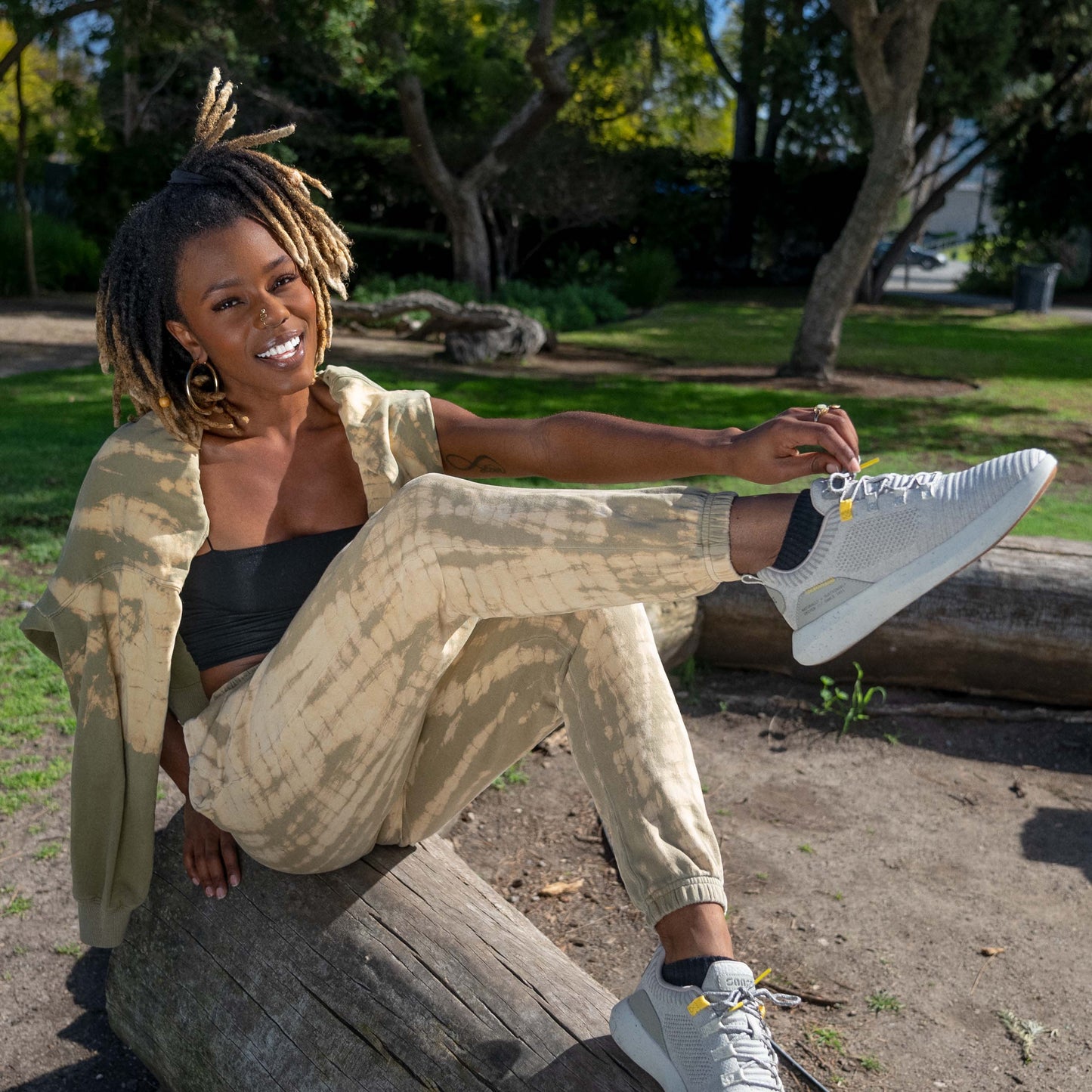 Lifestyle Image of young woman wearing sweats while sitting on a log and showing off her SNNCE Tabi sneakers