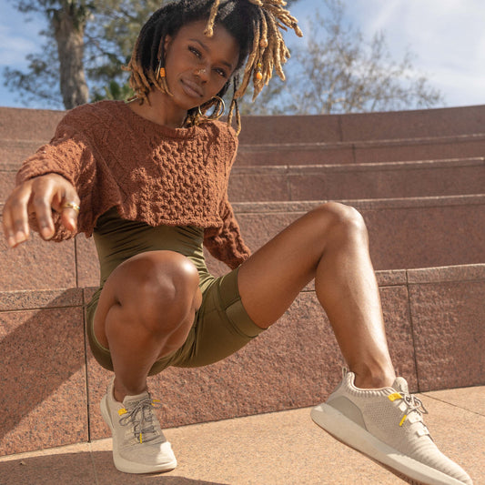 Lifestyle image of young woman kneeling wearing athletic apparel on outside steps looking into the camera while wearing SNNCE sneakers